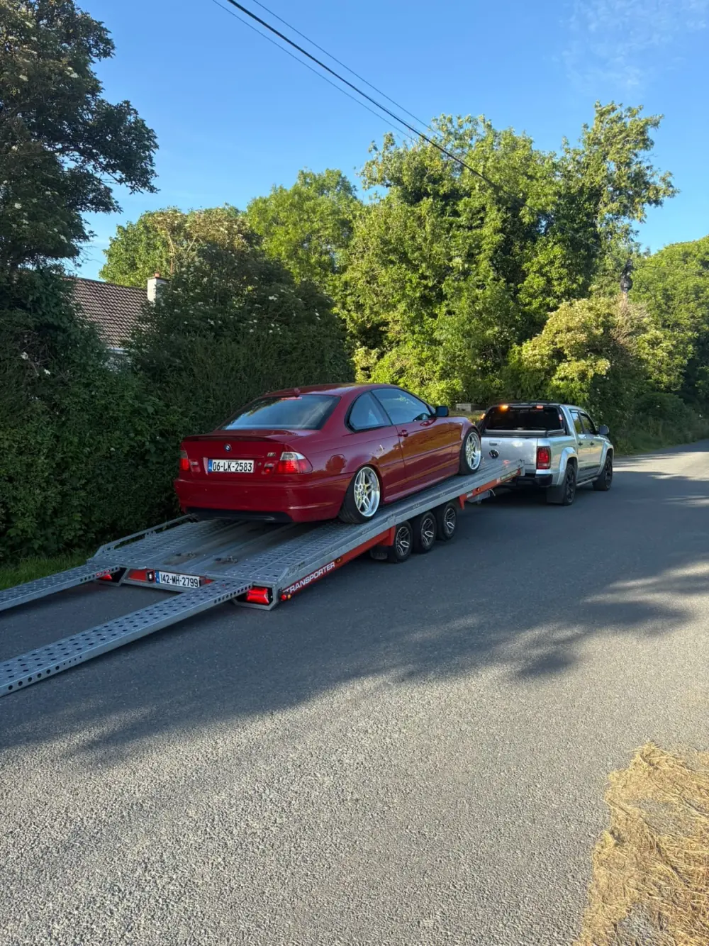 Red car loaded onto a vehicle transporter on a country road
